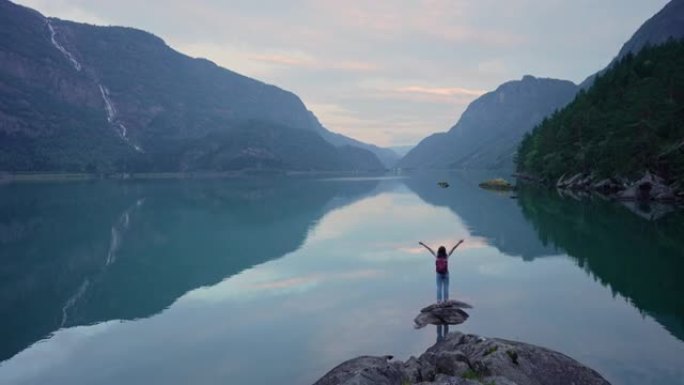 女人在挪威的湖泊背景上举手