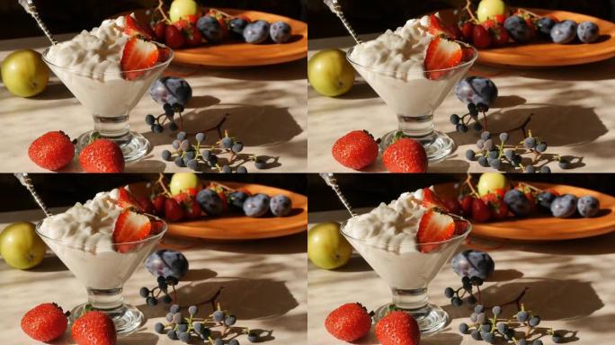 白色软冰淇淋，草莓和玻璃冰淇淋机中的银勺，腿放在桌子上，水果被午后的阳光照亮。奶油水果和浆果甜点