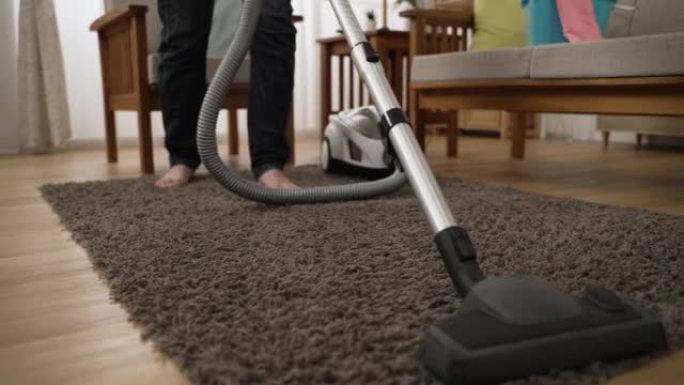 胡佛头清理客厅地毯的特写视图，一名赤脚清洁工站在家政日的背景下。