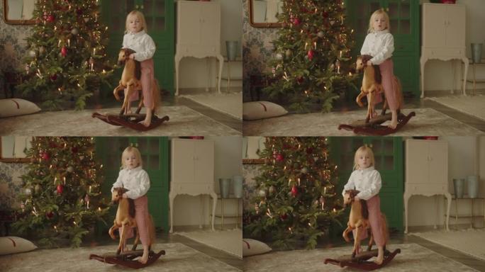 圣诞节前夕，金发小女孩独自坐在玩具马上。3-4岁的孩子，梦见礼物，父母在厨房里忙着等客人。