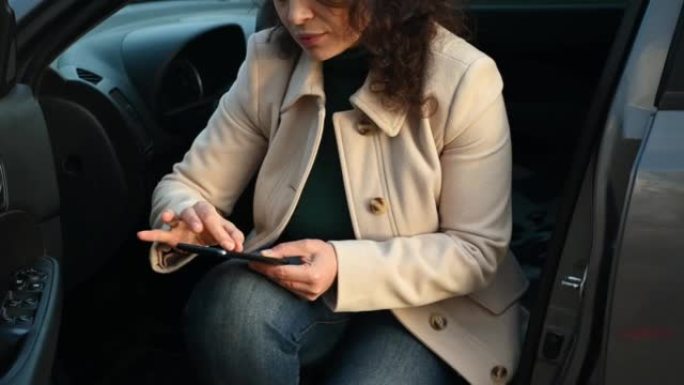 短镜头:穿着休闲装的女商人坐在车里的驾驶座上，用智能手机打电话给汽车服务公司
