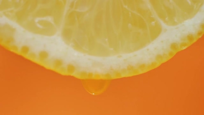 柠檬汁从果肉中流出，并在橙色背景上滴落，微距视频，慢动作