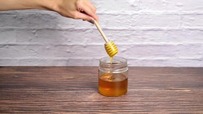 木制背景上带有蜂蜜铲斗的玻璃罐中的蜂蜜