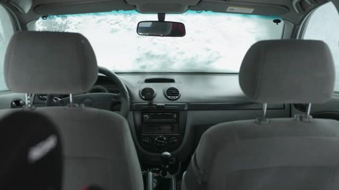 车主将汽车的挡风玻璃从雪地上清洗干净。