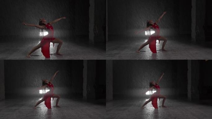 穿着红色连衣裙的诱人年轻女舞者在黑暗工作室的雨中表演