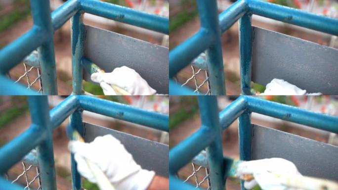 工人在铁质阳台施工栏杆上涂亮蓝色，人戴着防护手套，用油漆覆盖金属表面后生锈和腐蚀去除。刷新阳台外观，