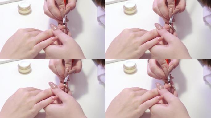 一个女孩在美容院修指甲的特写镜头。指甲护理。美甲师用白色清漆刷指甲的角。美容程序