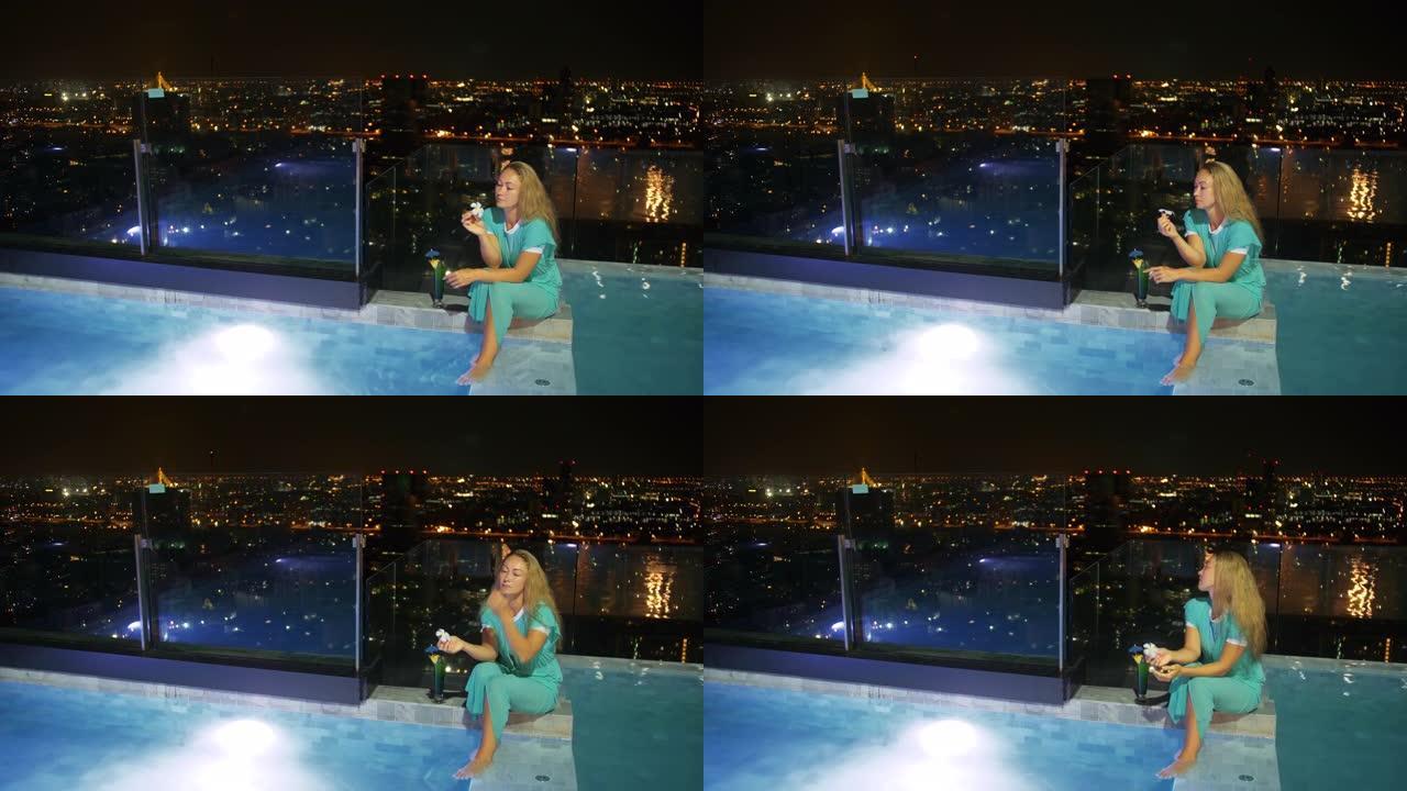 这位漂亮的女商人花时间在豪华酒店里。女人在屋顶照明游泳池的边缘放松，喝鸡尾酒。在现代夜大城市休息旅行
