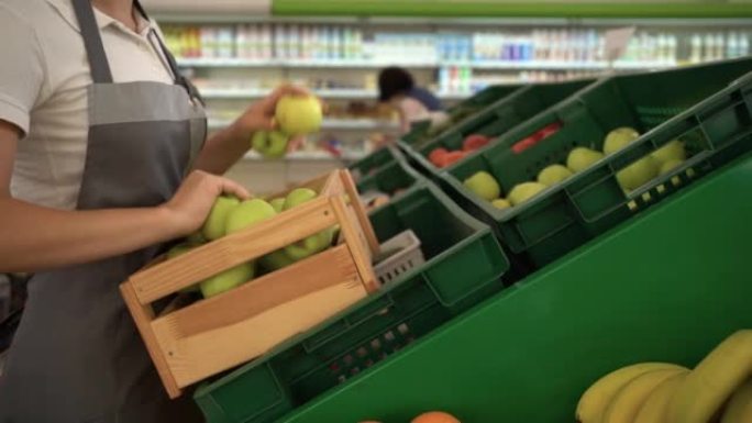 穿着围裙的女人在水果部超市的门市部工作。她在架子上摆放苹果。