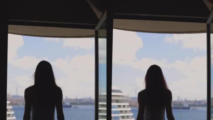 女人的剪影从酒店阳台看风景，一个穿着裙子的女人在酒店阳台上休息，看着大海和船的景色，女人打开窗帘