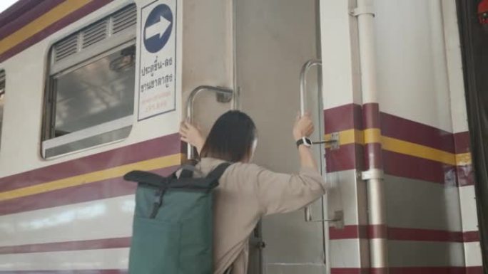 快乐的亚洲女人背包客蓝色背包为了安全抓住火车栏杆，踩着要旅行的火车。4k分辨率。