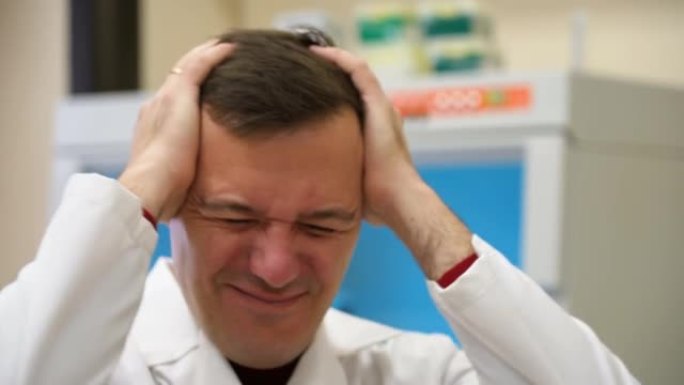 患有偏头痛头痛问题的千禧一代用手握着头。中年专业科学家男子穿着白大褂，手放在头上，因为实验室压力很大