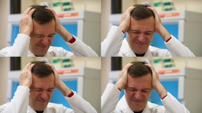 患有偏头痛头痛问题的千禧一代用手握着头。中年专业科学家男子穿着白大褂，手放在头上，因为实验室压力很大