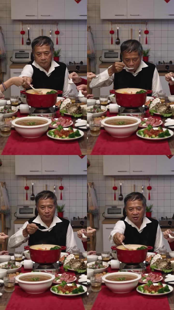 垂直屏幕: 亚洲大家庭晚上在家里聚在一起吃新年团圆饭时，用勺子吹着品尝热腾腾的美味汤