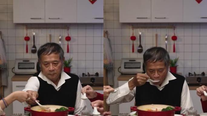 垂直屏幕: 亚洲大家庭晚上在家里聚在一起吃新年团圆饭时，用勺子吹着品尝热腾腾的美味汤