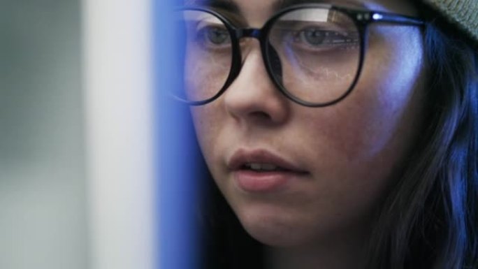 一位年轻漂亮的女商人戴着眼镜戴着帽子看着电脑屏幕的肖像，电脑屏幕上的交易图表反映在眼镜上。股票交易市