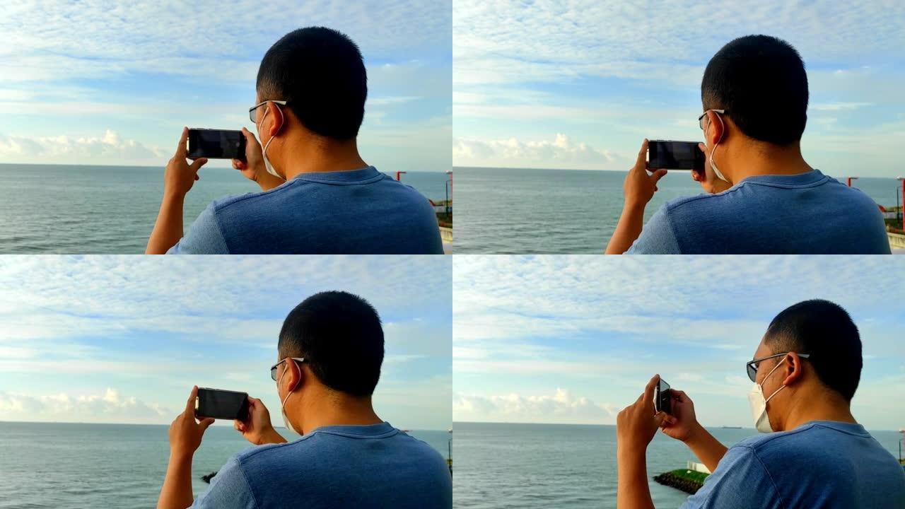 一名戴着面具的亚裔男子在手机上记录海滩美景的高清镜头
