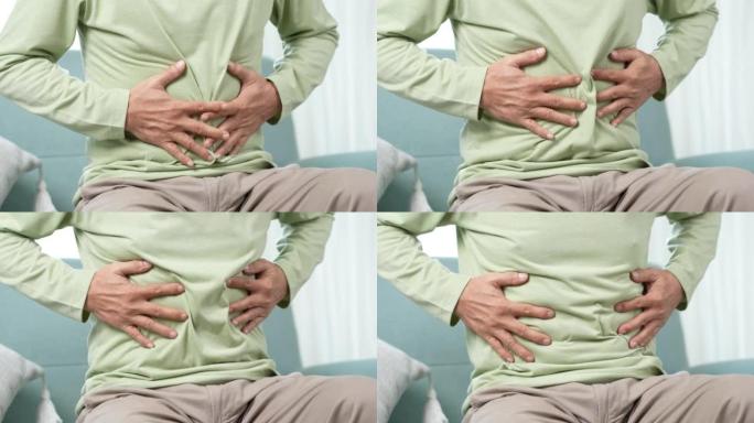 亚洲老人感到胃痛。年长的成熟男性在家坐在客厅的沙发上摸肚子。肠道问题医疗保健和医疗保险概念。