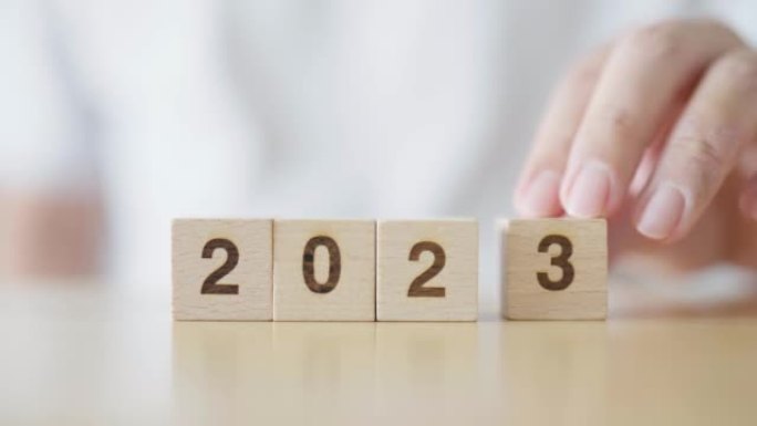 新的2022年变化2023年。用手把木方块和年号。新年决议，圣诞快乐