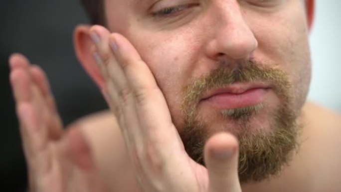剃刀剃须后，用润肤油抚平受刺激的面部皮肤，用手在镜子前按摩脸颊和胡须。剃须后的皮肤护理程序，男性美容