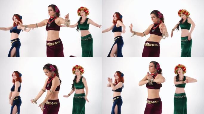 三个苗条的女人移动灵活的身体在白色背景下慢动作跳舞。集中自信的高加索肚皮舞者表演中东舞蹈，举起双手。