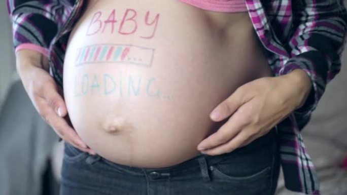 粉色和蓝色的婴儿加载铭文在女人怀孕的腹部，未来的妈妈秘密地抱着她的婴儿性别，女人用手关心她可爱的圆肚