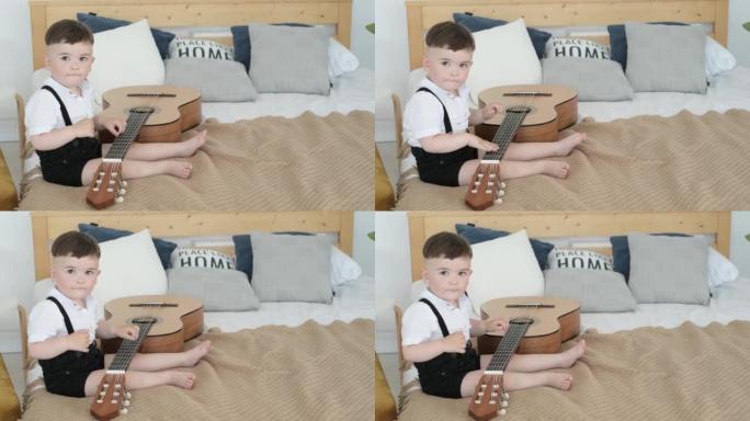 一个2岁的小男孩坐在床上弹吉他。一个孩子弹吉他。