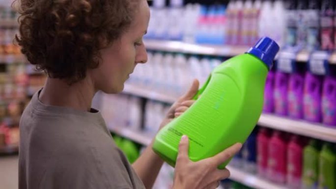 一位金发卷发的欧洲妇女在家用化学品部门选择洗衣粉作为家庭。一名妇女仔细检查洗涤凝胶的成分。
