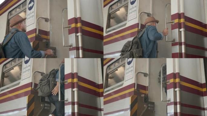 快乐亚洲英俊的背包客男子戴着帽子，牛仔夹克和背包抓住火车栏杆以确保安全，并踩在火车上旅行。4k分辨率