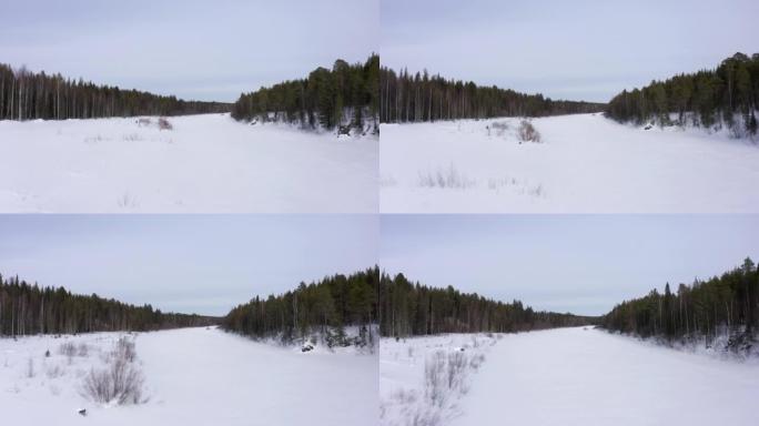 无人机在冰雪覆盖的森林中沿着冰冻的河床飞行