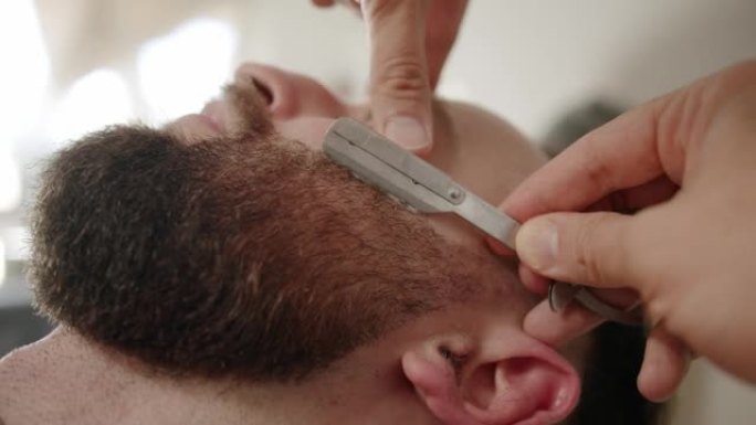 专业理发师用直剃刀刮顾客胡须。胡须切割