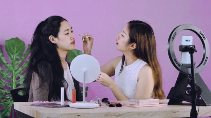 直播，视频4k的年轻亚洲女性化妆师vlogger在家里的网上商店录制智能手机相机展示的视频时，为漂亮