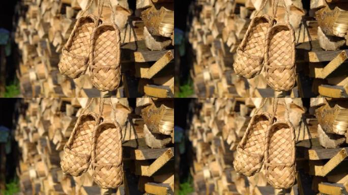 乡村乡村概念。柳条桦木树皮韧皮鞋挂在木柴的背景上。