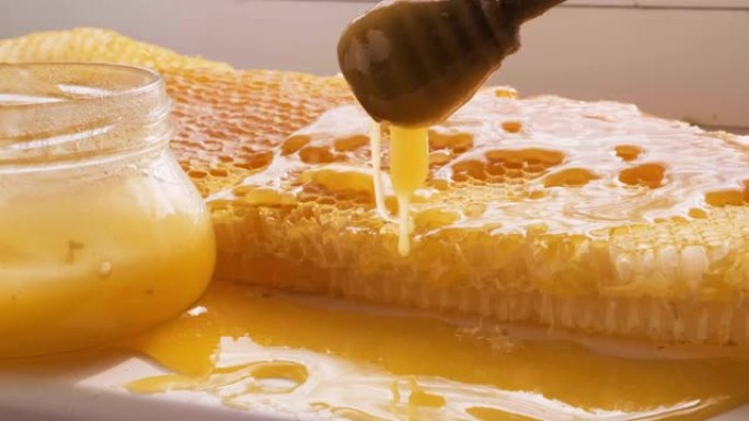 蜂蜜从蜂窝状框架上的蜜勺中滴落。天然液体蜂蜜从滴头流到蜂蜡碎片上。
