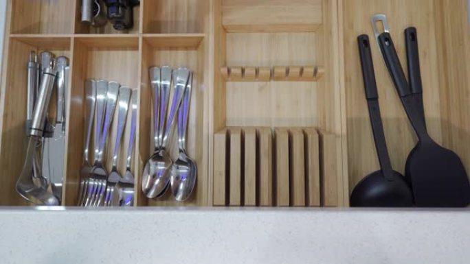 厨柜开放式抽屉，带餐具隔间，女人把叉子勺子放在竹木餐具收纳器里。餐具储物托盘特写。