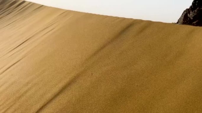 沙丘沙漠沙滩抽象镜头。沙粒在风中飘扬。阳光反射在折叠的沙子表面上。