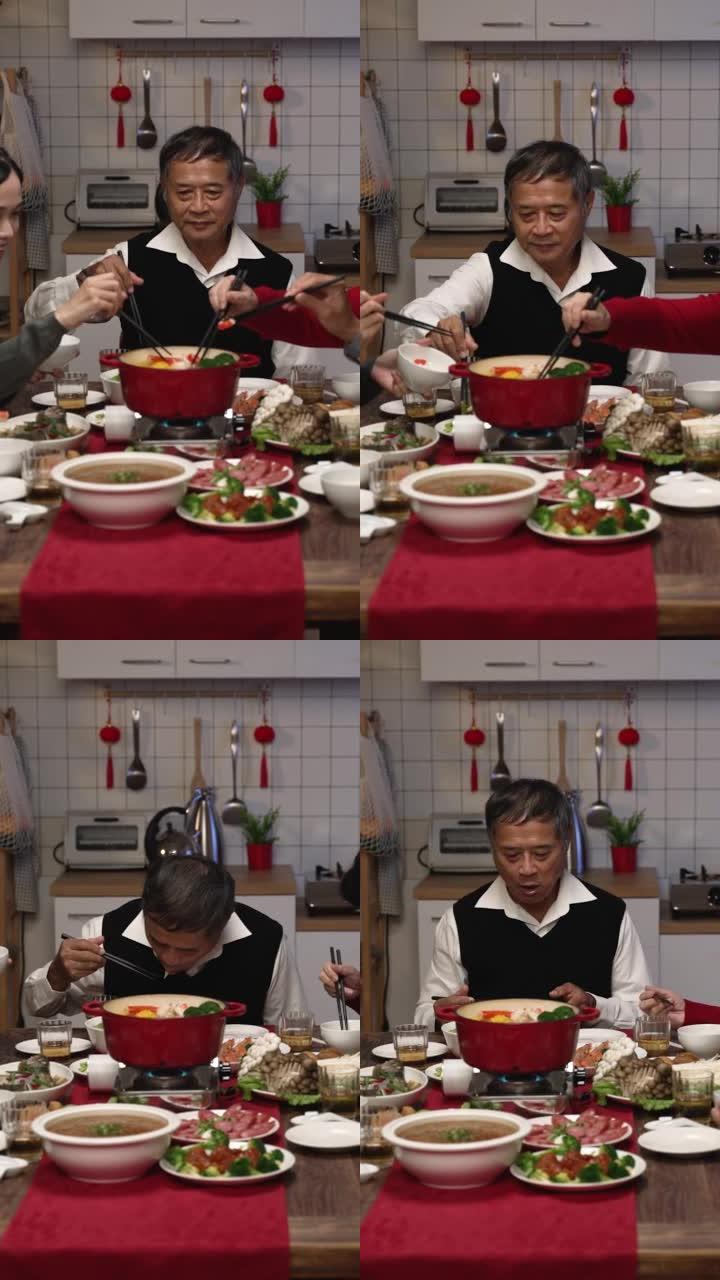 垂直屏幕: 快乐的亚洲家庭成员在农历除夕在家享用传统的团圆饭时，用筷子从火锅中采摘食物
