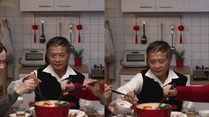 垂直屏幕: 快乐的亚洲家庭成员在农历除夕在家享用传统的团圆饭时，用筷子从火锅中采摘食物