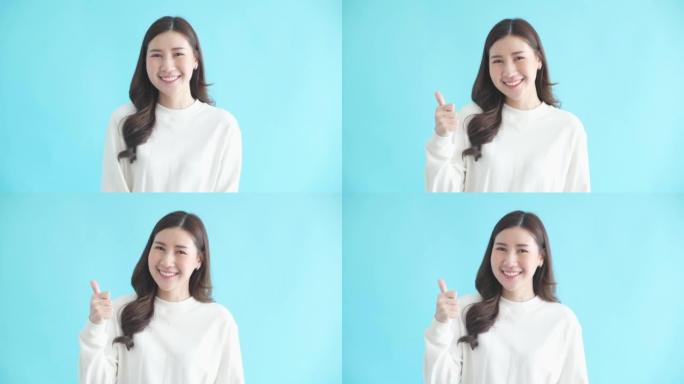 快乐美丽的亚洲女人展示拇指向上的标志，微笑着看着相机，站在孤立的蓝色背景上，4k分辨率