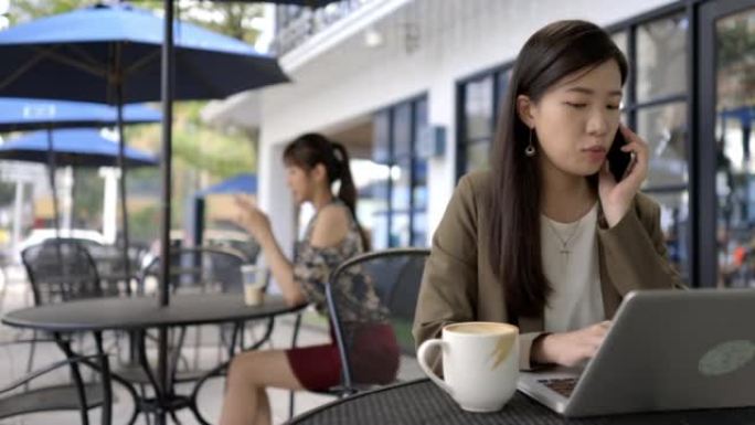一名年轻的亚洲妇女在外面的桌子上使用智能手机和笔记本电脑