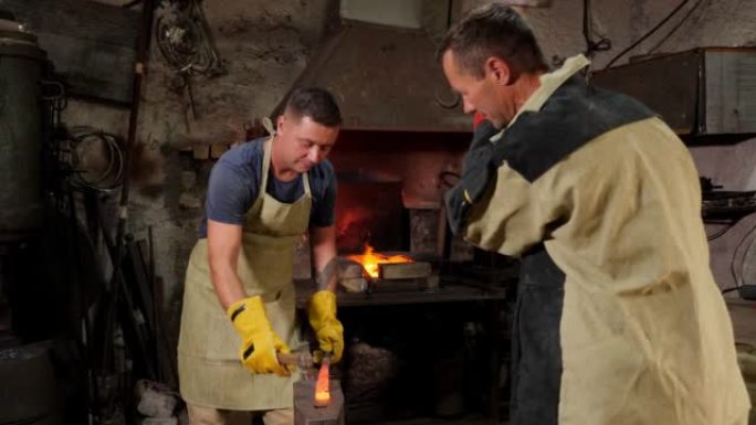 两个铁匠在铁砧上用铁锤敲打铁锤。