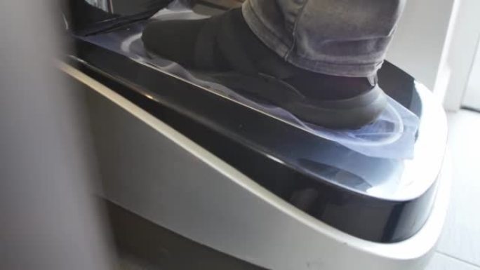 一只穿着街鞋的男性脚的特写镜头放在医疗诊所入口处的自动收缩鞋层压机中。在检疫期间，为了安全起见，有必