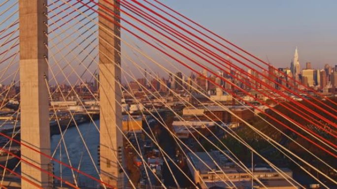 在阳光明媚的清晨，围绕威廉斯堡工业区的Kosciuszko桥的鸟瞰图，背景是曼哈顿的遥远景色。带有平