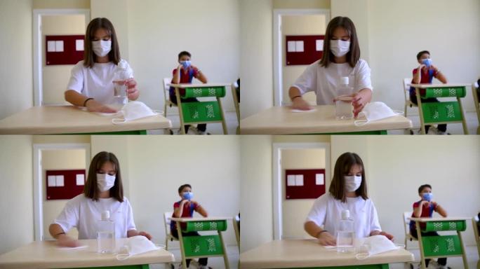 带口罩的女学生在教室里清洁手和带消毒抗菌凝胶的桌子
