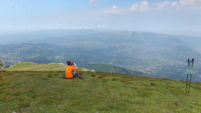 一名男子坐在草木山顶上喝水的高清镜头