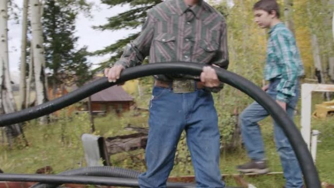 在美国科罗拉多州的一个小镇家庭拥有的牧场上，高加索牧场主的青少年一起工作，为农业移动一定长度的柔性塑