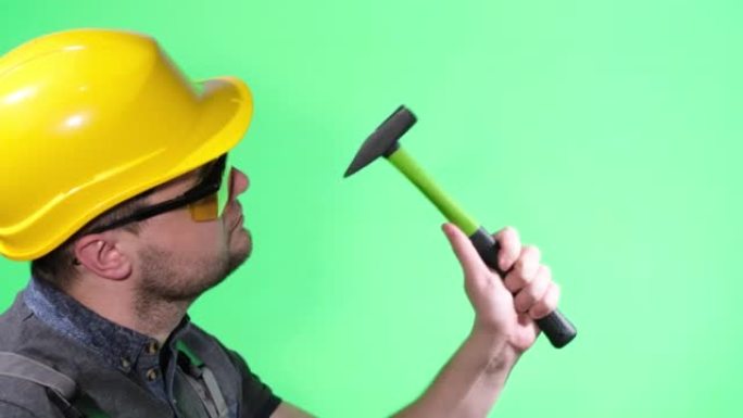 穿着黄色头盔和护目镜的男性建造者，用锤子工作，绿色背景上的chromakey，