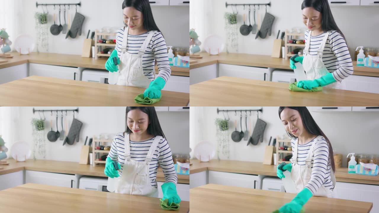 年轻的亚洲妇女用抹布喷洒和清洁桌子。漂亮的清洁服务工人家政和整理厨房