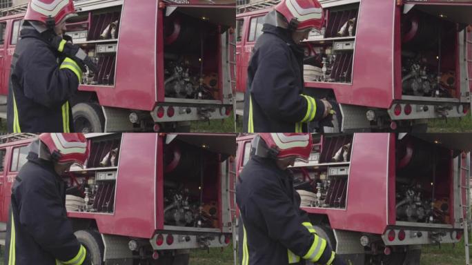 身穿防护服和头盔的消防队员站在消防救援车前准备装备。