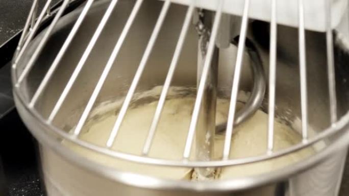 比萨饼或面包的面团在面团搅拌机中揉捏。摄像机通过金属网格从上方拍摄。